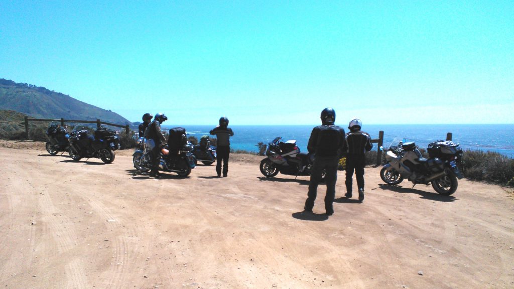 Motorcycle riders at a pull out on California Highway 1 on a sunny day overlooking the blue Pacific Ocean