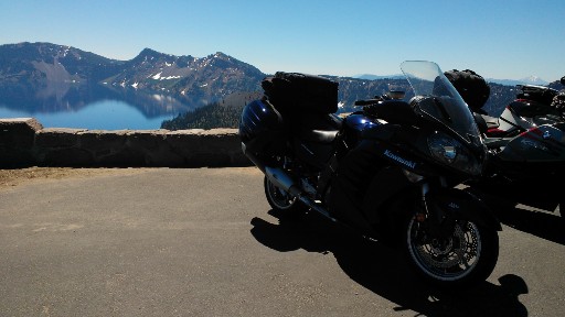 A motorcycle on the overlook above Crater Lake with the clear blue lake below   