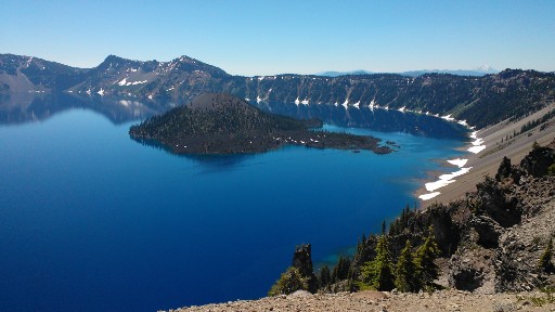 Crater Lake from an overlook ringed by pockets of snow at the base of the crater ridges  