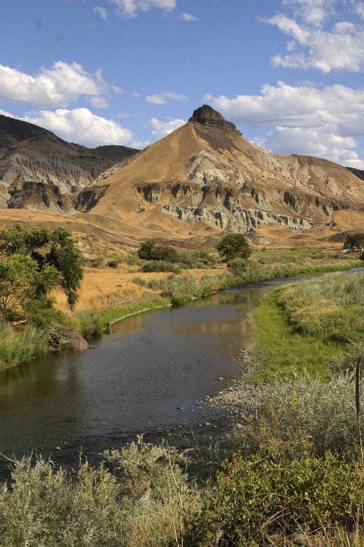 The john Day River passes through grass covered hills against a blue and white sky