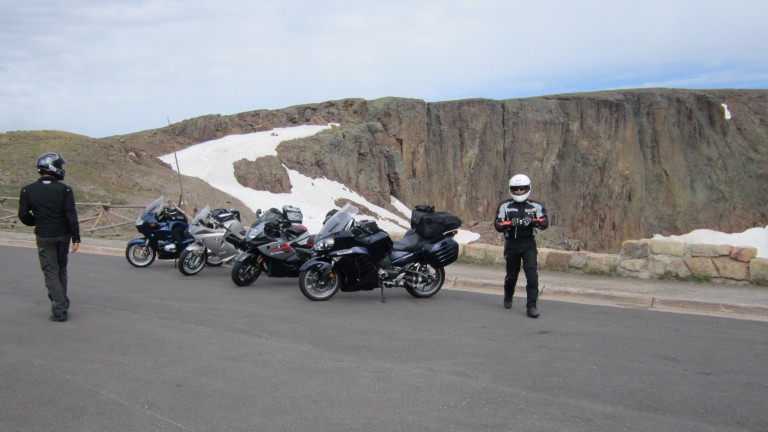 Geared up sport touring motorcycle riders at the summit with snow in the background in Rocky Mountain National Park  