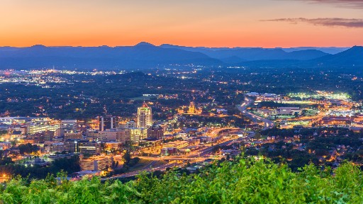 The city of Roanoke at dusk with orange sky and blue mountains in the distance 