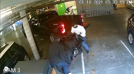 Two men in an und3rground parking garage lifting a motorcycle into the back of a pickup   