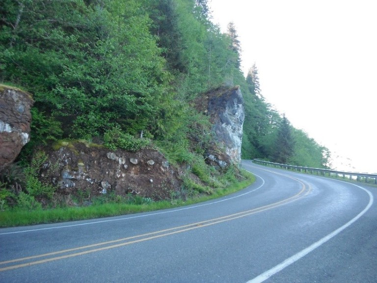 A twisty section of the Strait of Juan de Fuca Scenic Byway between a natural rock wall and the ocean below.    