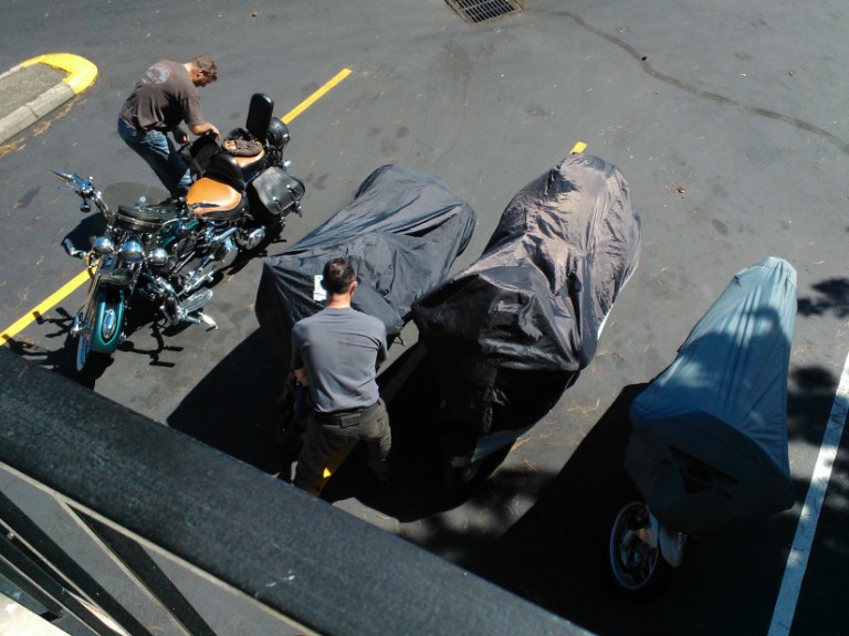 Two guys covering their motorcycles.