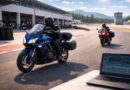 Two sport touring motorcycles on a sunlit racetrack near the pit lane, with telemetry data displayed on a laptop in the foreground.