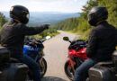 Two sport touring riders stopped on a mountain road, one gesturing ahead while discussing riding strategy with the other.